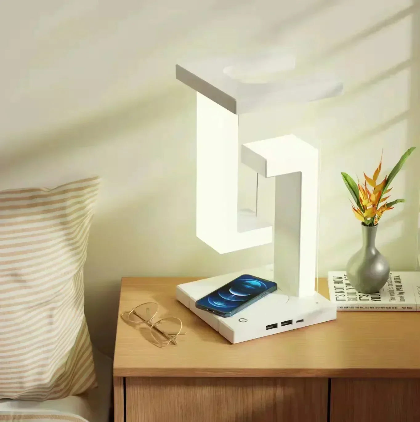 Floating LED lamp with wireless phone charging on a wooden bedside table.